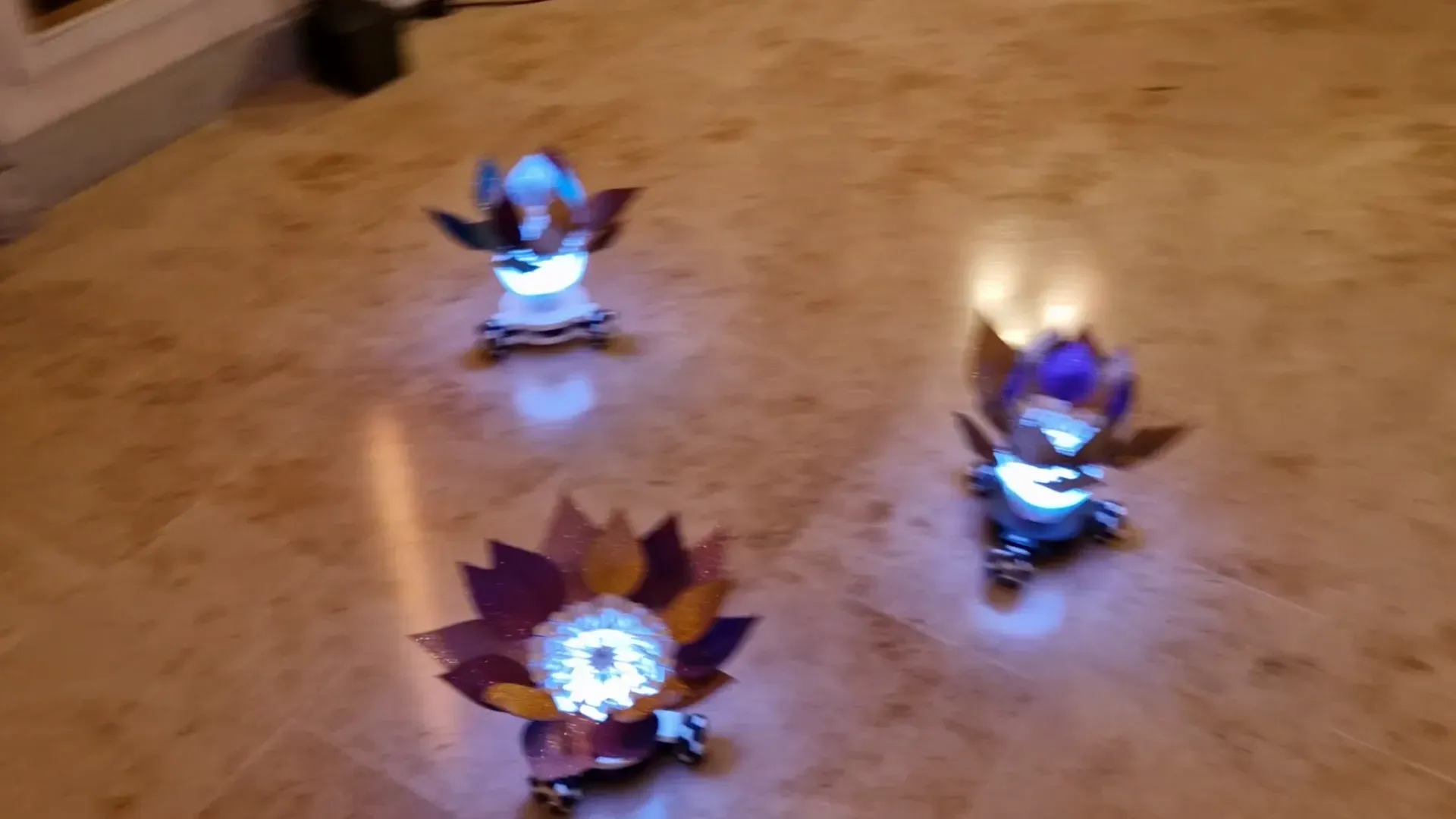 Three robots with bronze and purple petals rolling across the marble floor, close up